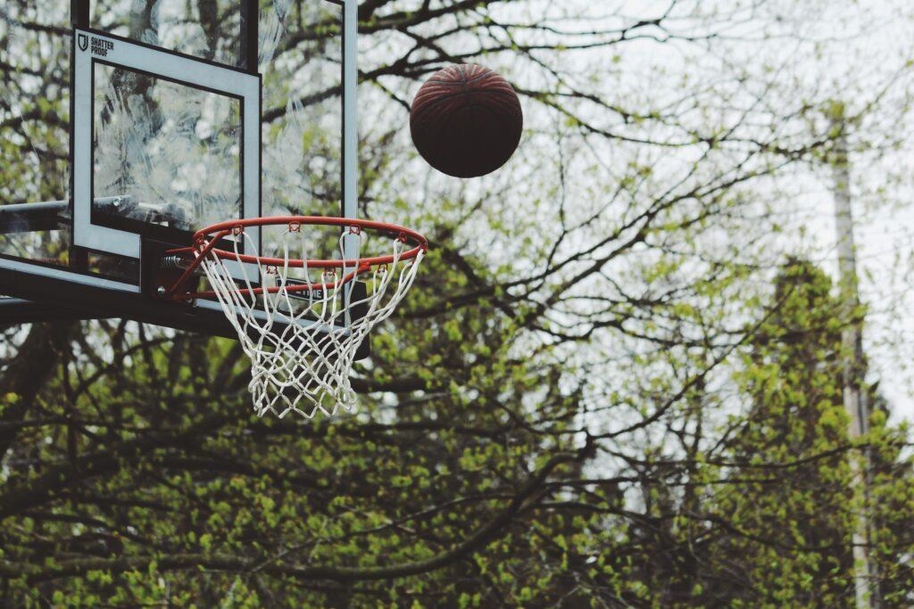 Basketball soaring toward hoop in outdoor court with trees in background.