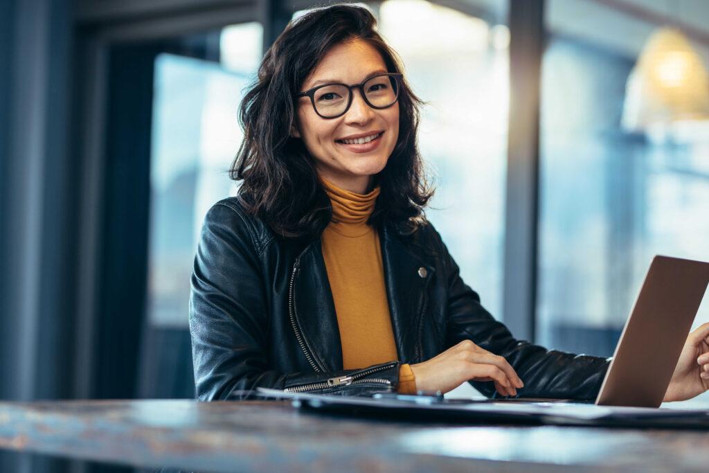 Smiling woman working on a laptop at a conference table.