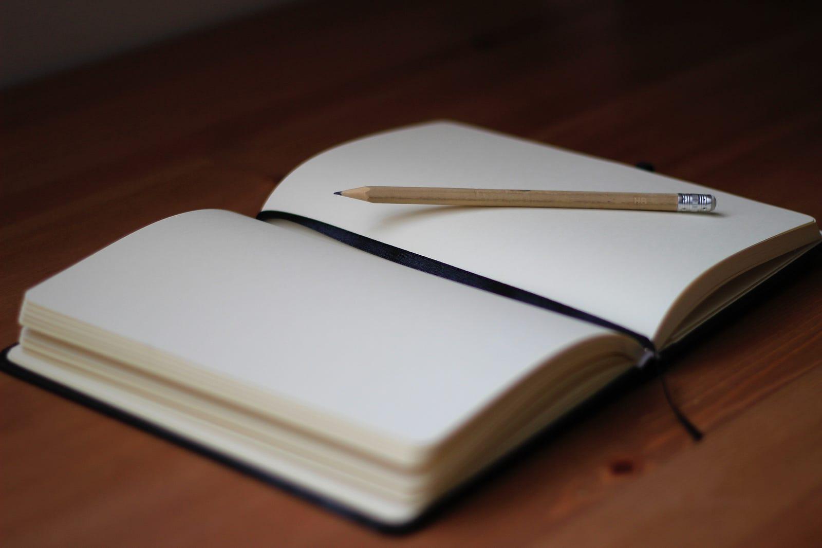 a journal sitting open on a wooden surface with a pencil on top